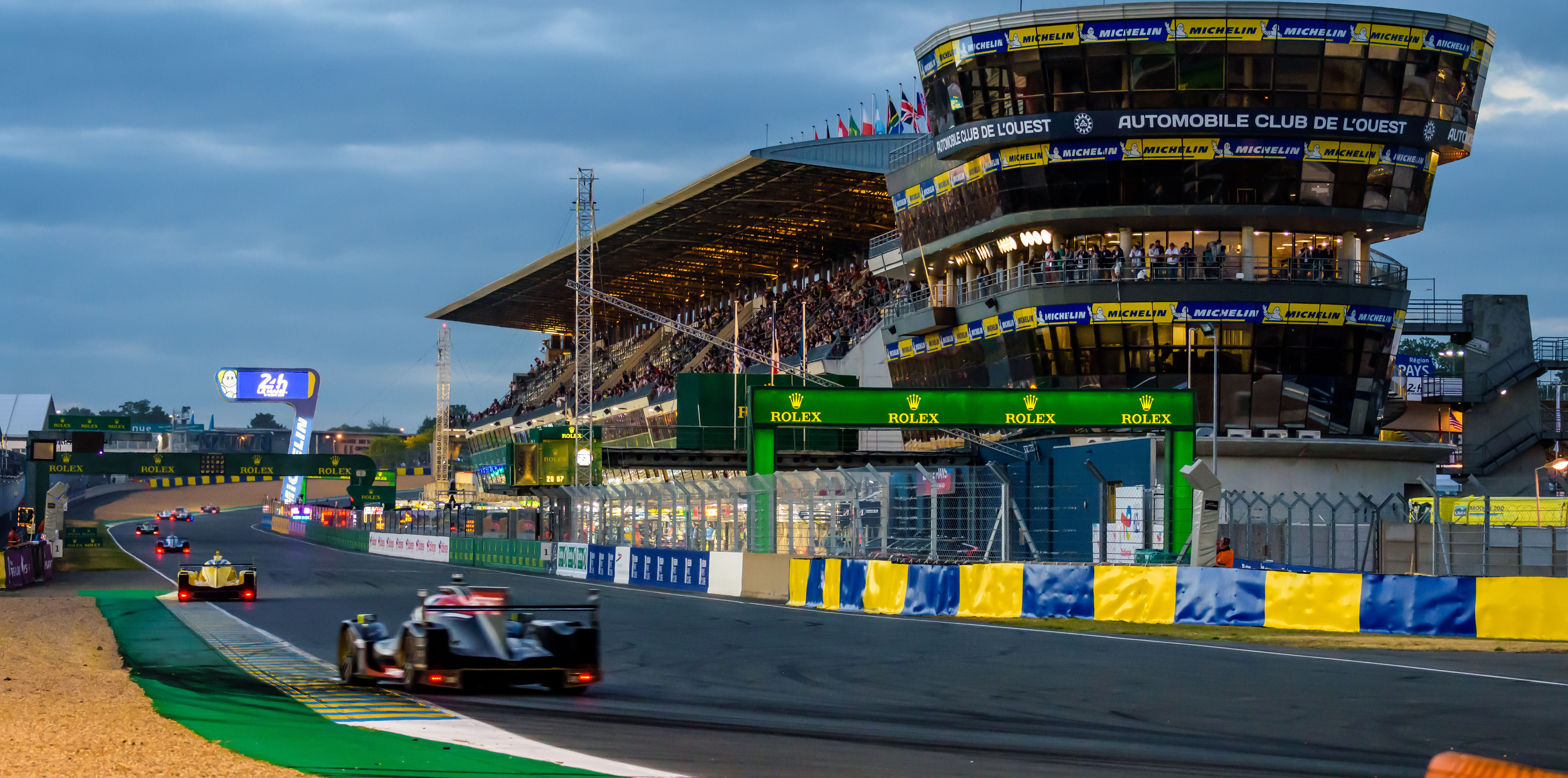 Race cars in the pit straight of the 24 hours of Le Mans at nightfall.